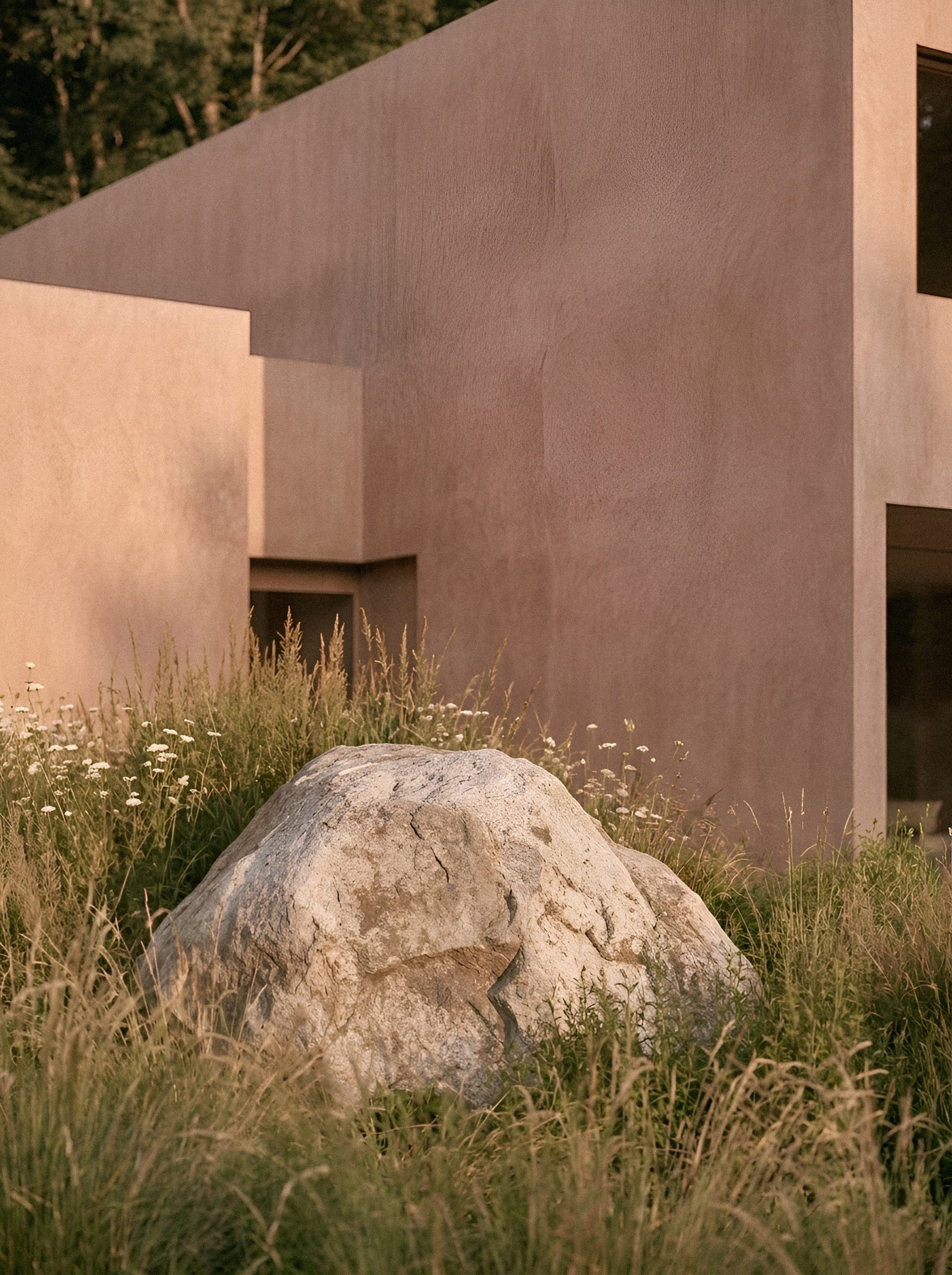 A large boulder beside a pink wall and garden grasses.
