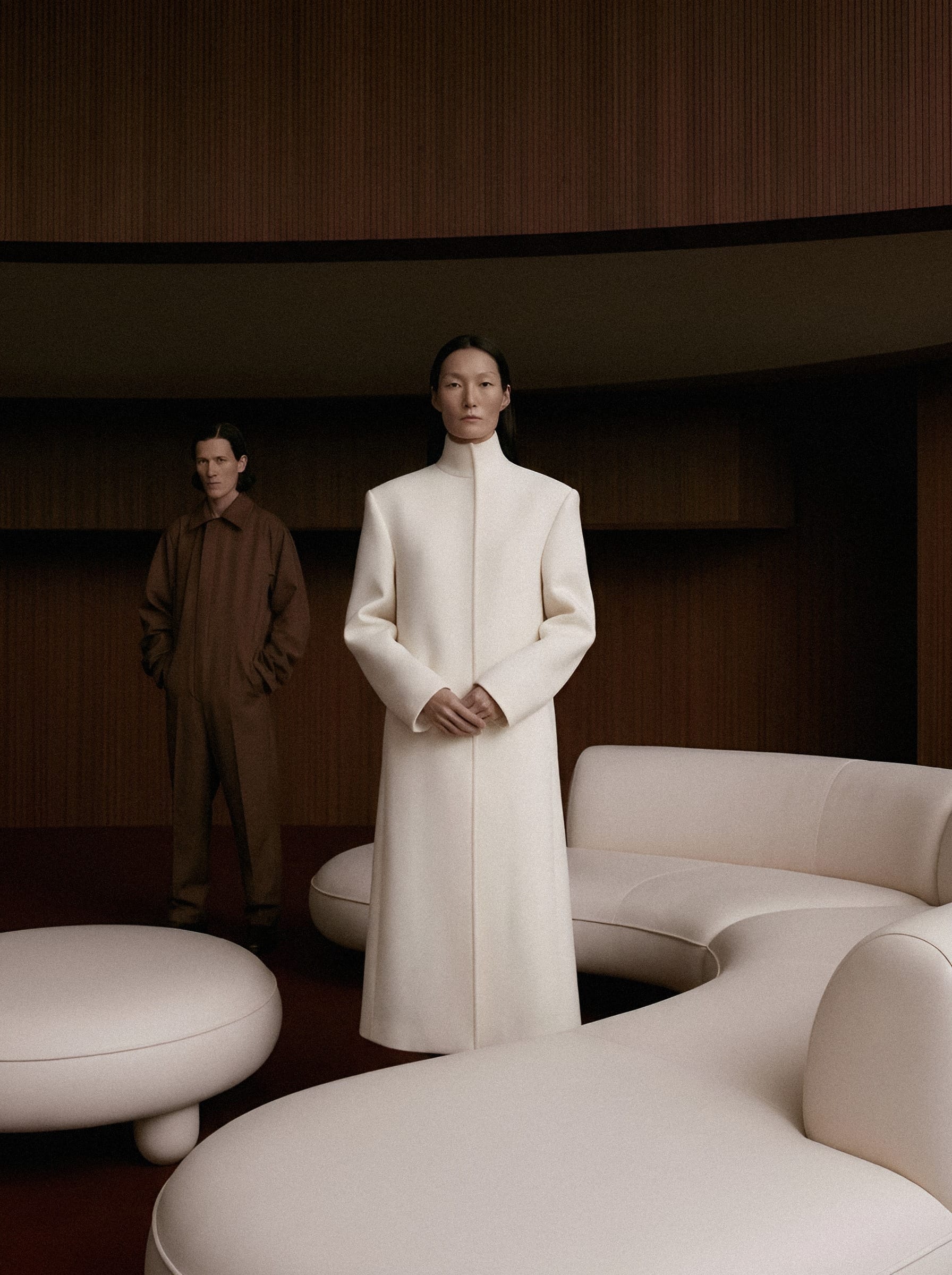 Two figures in cream and brown within a sculptural interior.
