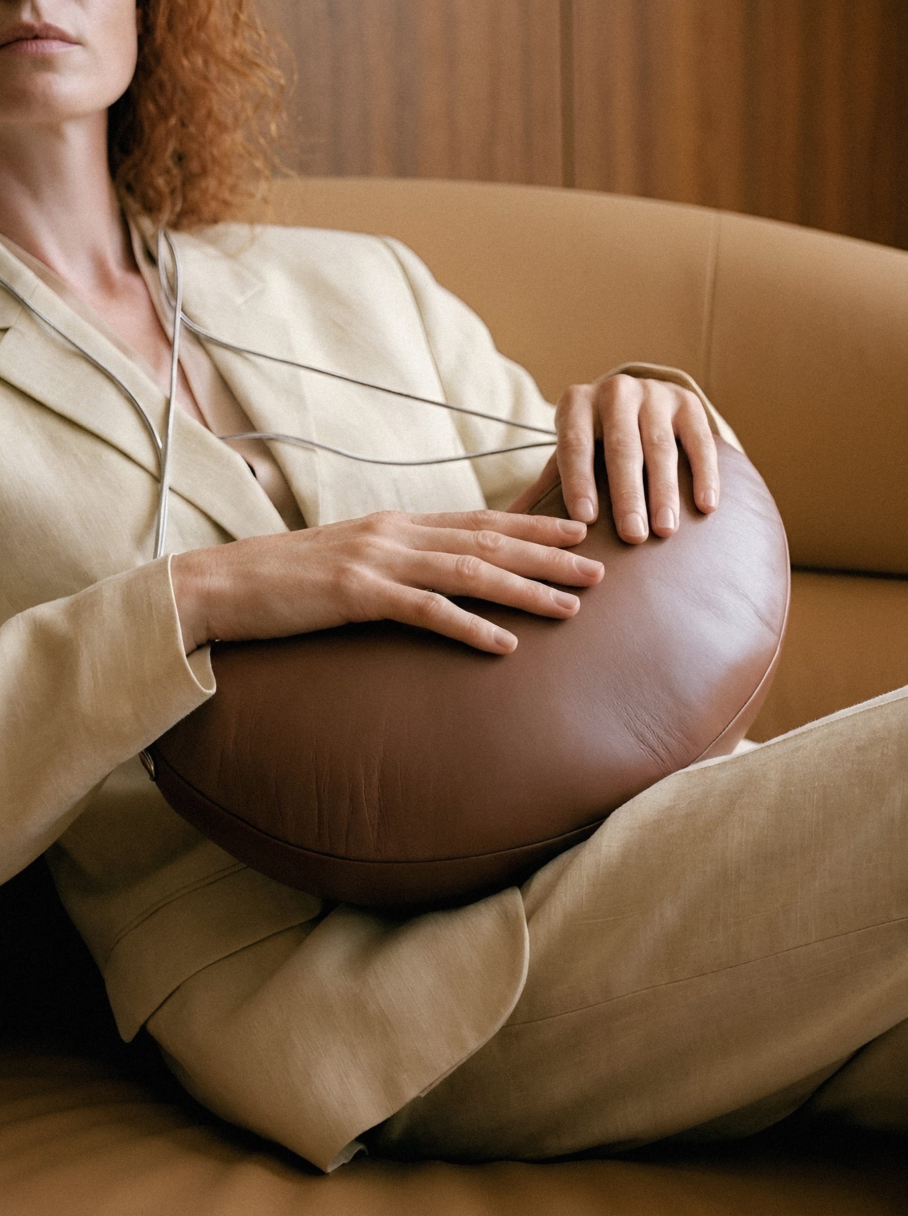 Hands holding a rounded brown leather cushion on a seated lap.
