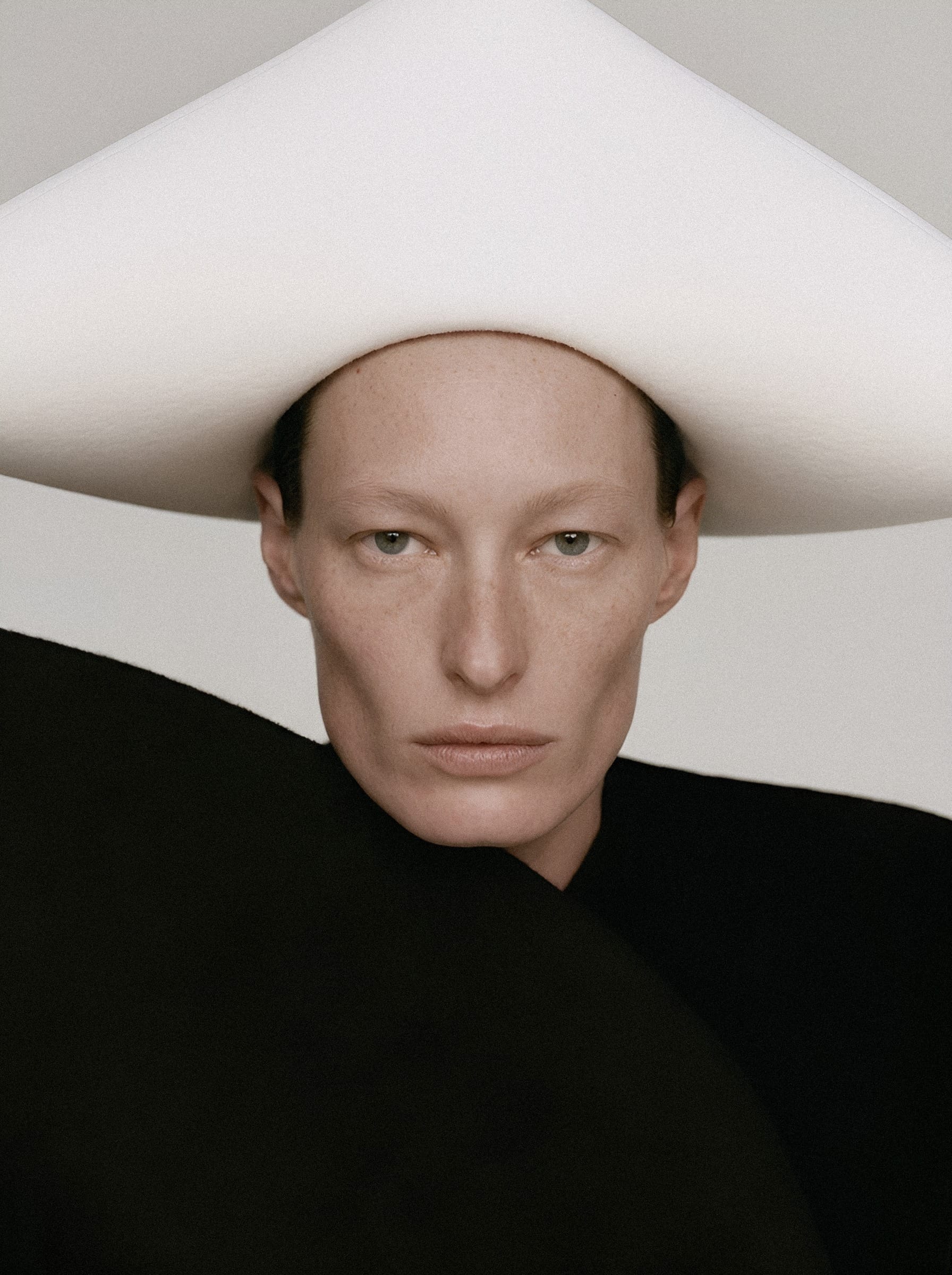 A portrait beneath a large angular white hat and sculpted black collar.
