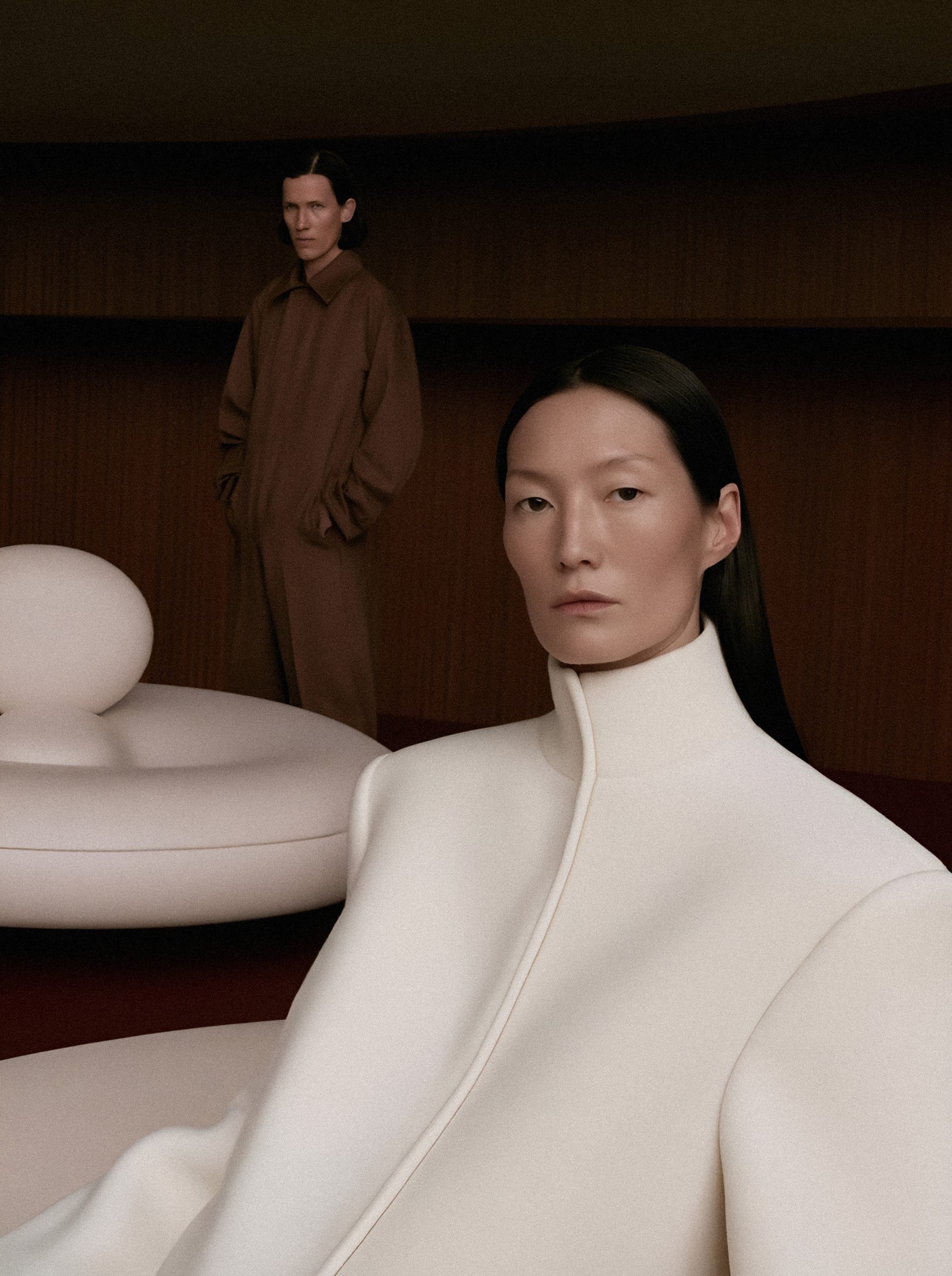 A woman in a white coat with another figure against a warm wooden interior.