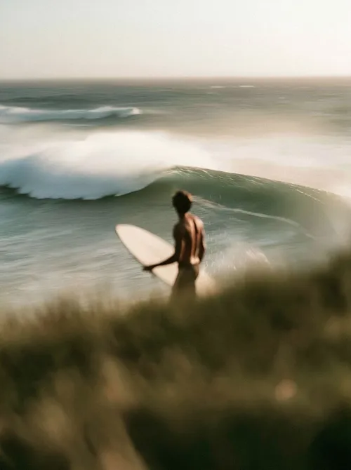 Surfer entering water at dawn.